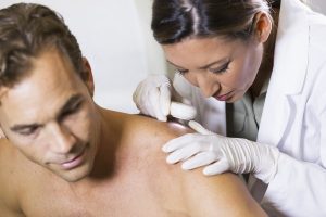 Dermatologist examining a mole on a male patient's shoulder