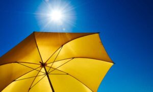 A yellow sun umbrella opened up against a blue, sunny sky