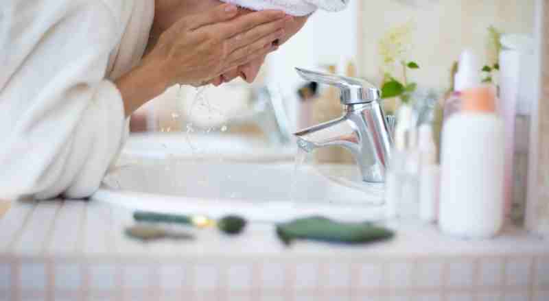 A woman is washing her face at a bathroom sink highlighting part of her skincare routine for after menopause