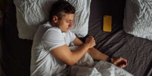 Man sleeping in bed with phone next to him, quality-night-of-sleep