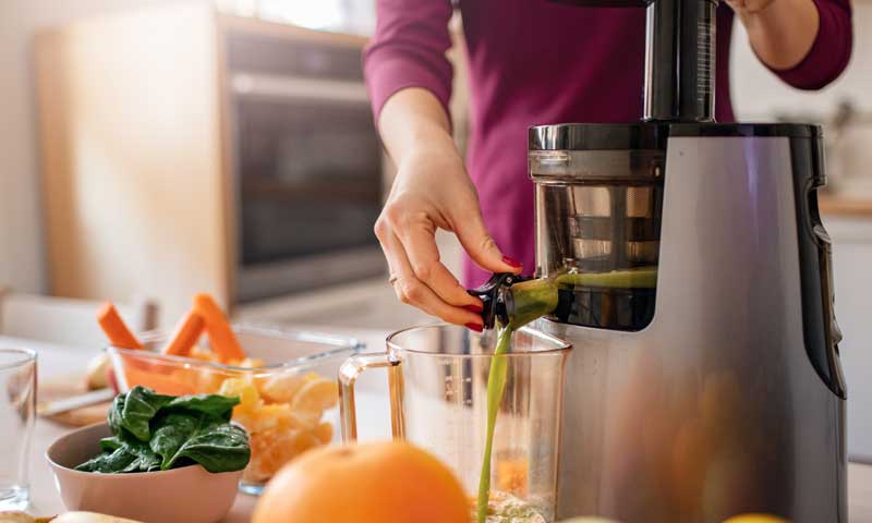Woman operating a cold press juicer using fresh vegetables and fruits