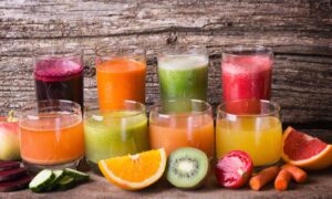 Eight glasses filled with fresh fruit juices and their fresh ingredients in front of themq