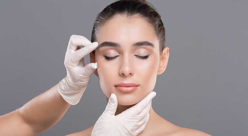 A woman’s face is being looked at by an aesthetician or doctor