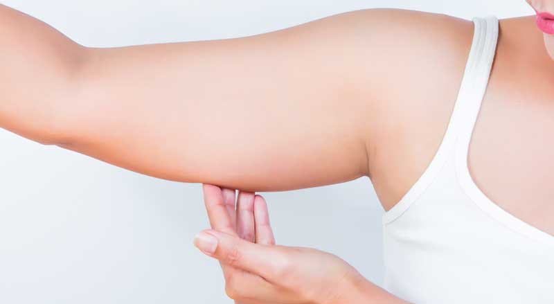 A woman looking at and touching the extra fat on her upper arm