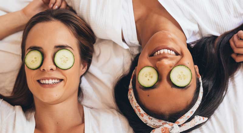 Two young women relaxing with cucumber slices on eyes to reduce dark circles under their eyes