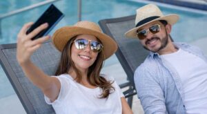 A man and a woman in sunglasses and hats taking a selfie