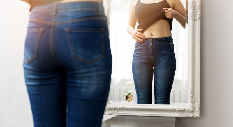 A woman looking at her bare abdomen in the mirror