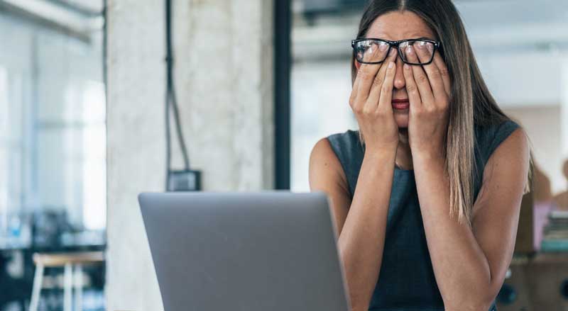 A woman at a computer is rubbing her eyes