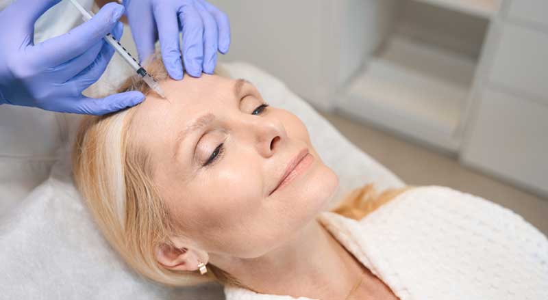 A smiling middle-aged woman is receiving a Botox injection