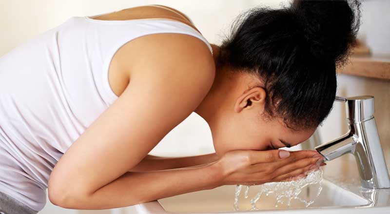 A woman washing her face at a bathroom sink