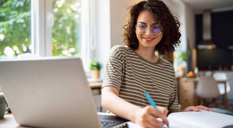 A young woman looks at a computer as she takes notes