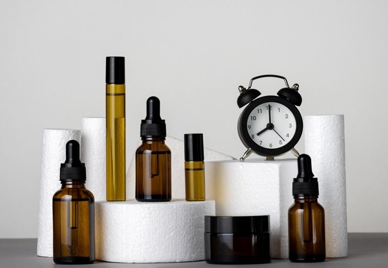 A table with a clock and different bottles of oils and skincare products illustrating the importance of timing when it comes to your skincare routine