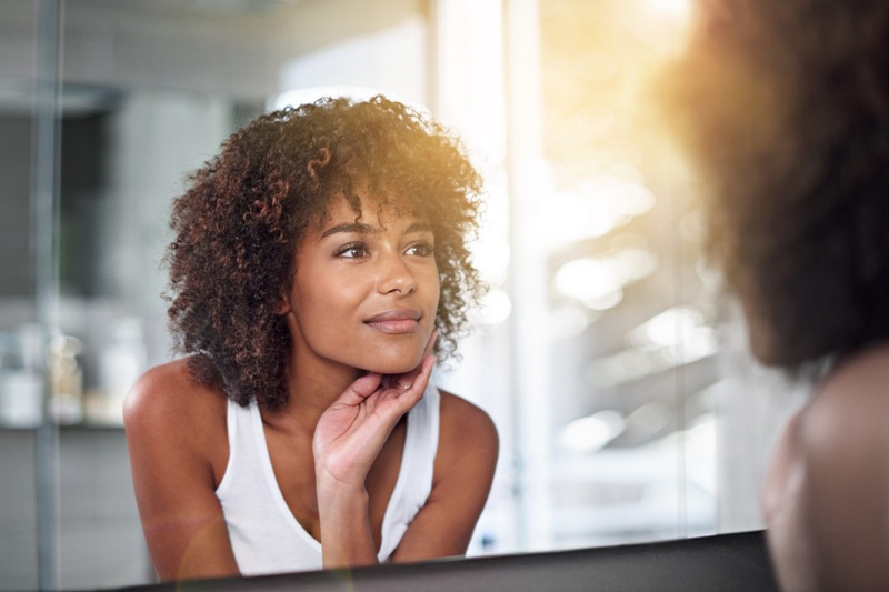 A woman gazes into a mirror, satisfied with the results she sees from changing her skincare routine due to her new understanding of her skin's natural patterns