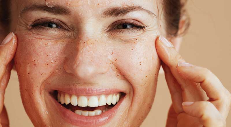 A smiling woman rubbing an exfoliant over her face