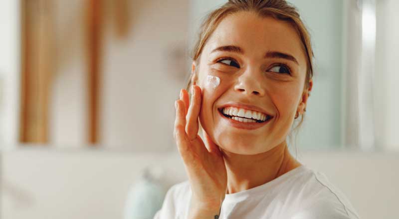 Young woman smiling and putting cream on her face